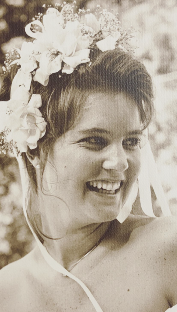 A woman with flowers and ribbons in her hair smiles brightly, looking to the side. The image is sepia-toned, giving it a vintage, timeless feel.