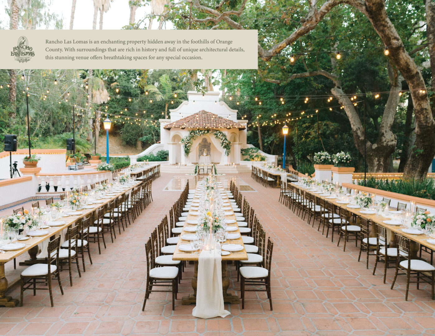An outdoor wedding venue with long dining tables, wooden chairs, string lights, and a white gazebo surrounded by lush trees and greenery at Rancho Las Lomas.